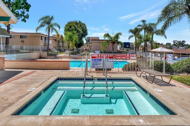 community pool with a community hot tub, fence, and a residential view