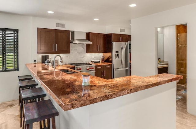 kitchen featuring sink, wall chimney exhaust hood, stainless steel appliances, kitchen peninsula, and a breakfast bar area