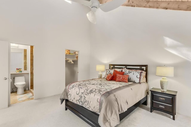 bedroom featuring ceiling fan, ensuite bathroom, a towering ceiling, and light colored carpet