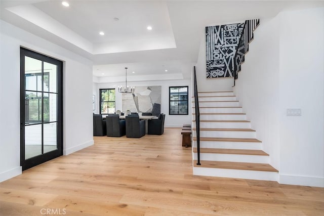 staircase with a raised ceiling, hardwood / wood-style floors, and an inviting chandelier