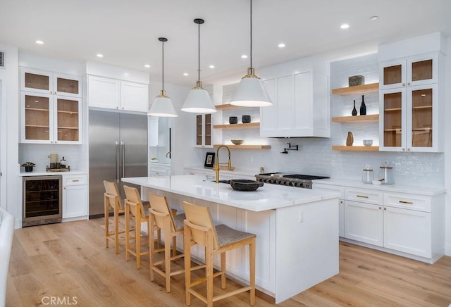 kitchen with stainless steel appliances, beverage cooler, light hardwood / wood-style floors, white cabinetry, and an island with sink