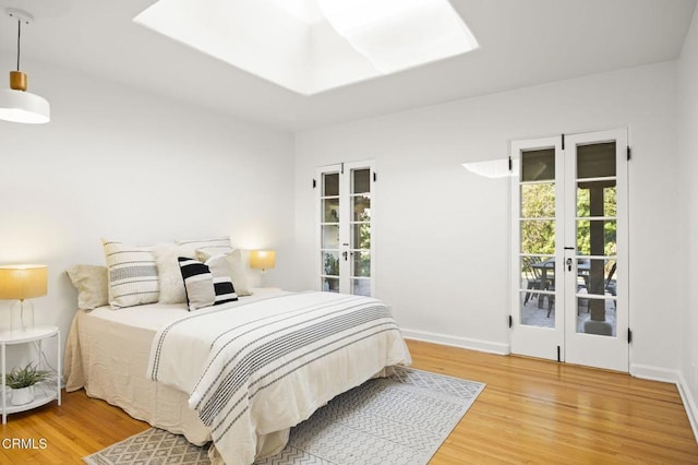 bedroom featuring french doors, baseboards, a skylight, and light wood finished floors