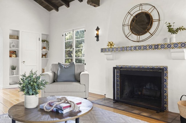 living room with a tiled fireplace, beamed ceiling, and wood finished floors