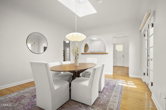 dining area featuring light wood-style flooring, a skylight, and baseboards