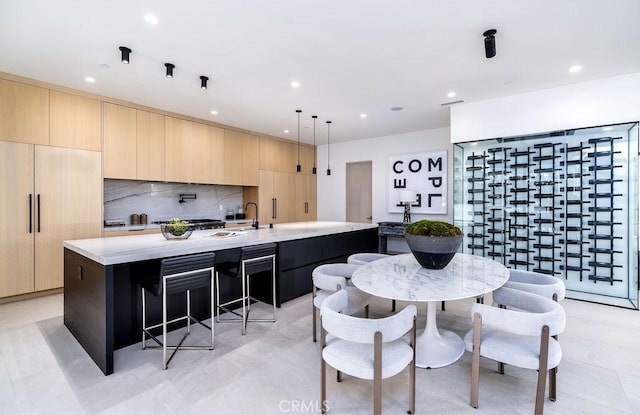 kitchen featuring hanging light fixtures, light brown cabinets, tasteful backsplash, and a kitchen island with sink