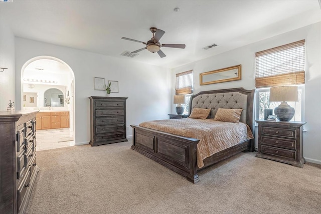 bedroom featuring ceiling fan, light colored carpet, connected bathroom, and multiple windows