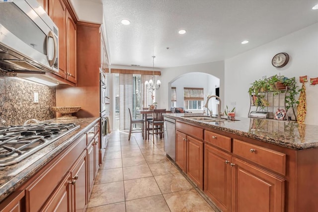 kitchen with sink, decorative light fixtures, a center island with sink, dark stone counters, and stainless steel appliances