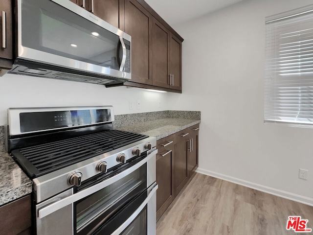 kitchen with appliances with stainless steel finishes, dark brown cabinetry, light hardwood / wood-style flooring, and light stone counters