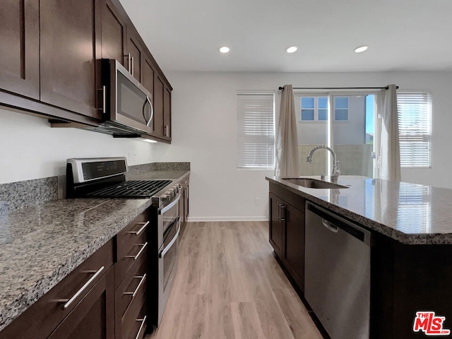 kitchen featuring light stone countertops, light wood-type flooring, stainless steel appliances, and sink