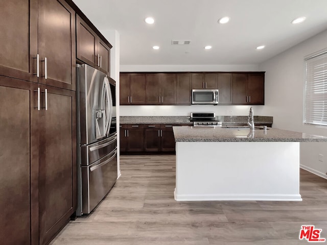 kitchen with sink, stainless steel appliances, an island with sink, and light hardwood / wood-style flooring