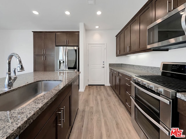 kitchen with light stone countertops, appliances with stainless steel finishes, dark brown cabinetry, sink, and light hardwood / wood-style floors