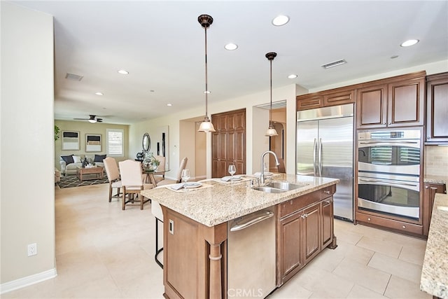 kitchen featuring pendant lighting, sink, a center island with sink, appliances with stainless steel finishes, and light stone countertops