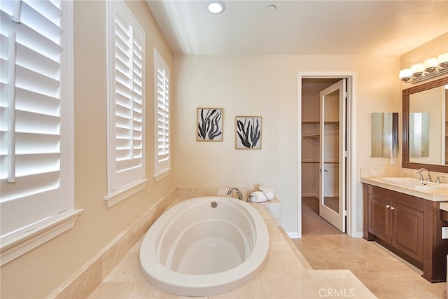 bathroom with tiled tub, vanity, and tile patterned flooring