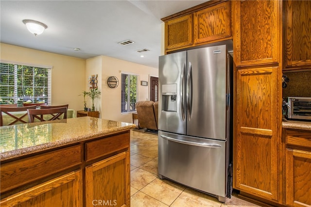 kitchen with stainless steel refrigerator with ice dispenser, light stone countertops, and light tile patterned floors