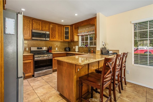 kitchen featuring sink, kitchen peninsula, backsplash, appliances with stainless steel finishes, and a kitchen breakfast bar