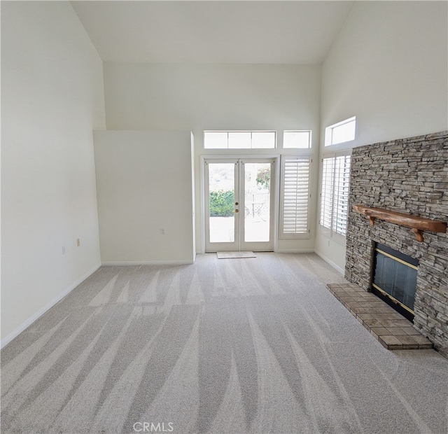 unfurnished living room with french doors, light colored carpet, a fireplace, and a towering ceiling