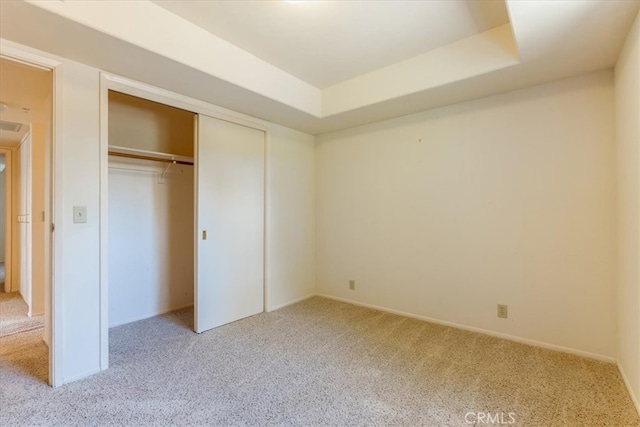 unfurnished bedroom featuring a raised ceiling, light carpet, and a closet