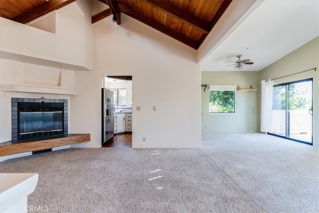 unfurnished living room featuring carpet floors, beamed ceiling, a tiled fireplace, and ceiling fan