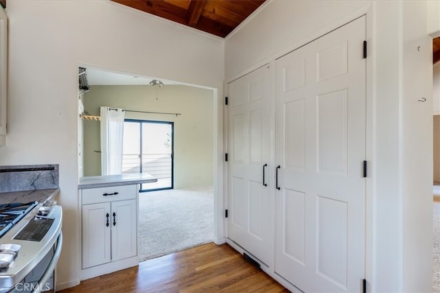 kitchen with vaulted ceiling with beams, white cabinets, stainless steel stove, wooden ceiling, and light hardwood / wood-style floors