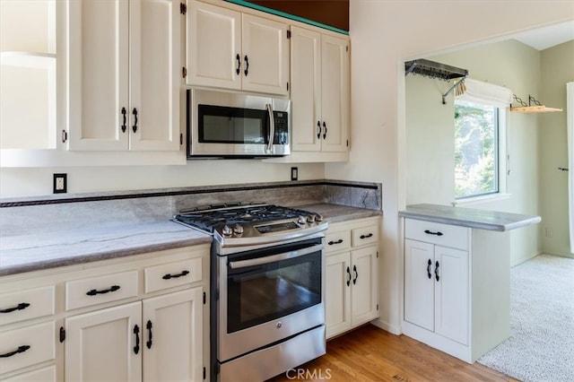 kitchen with stainless steel appliances, light hardwood / wood-style floors, and white cabinetry