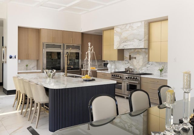 kitchen featuring sink, a kitchen island with sink, a kitchen breakfast bar, decorative backsplash, and appliances with stainless steel finishes