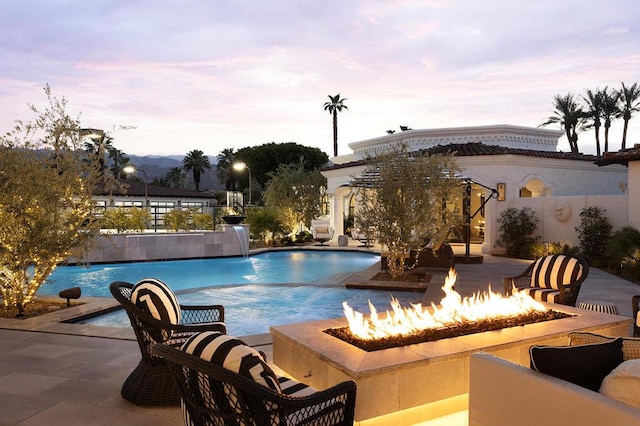 pool at dusk with a patio area, pool water feature, and a fire pit