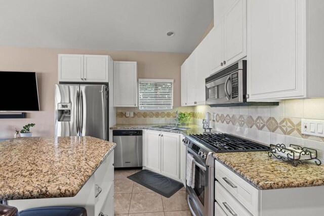 kitchen with light tile patterned floors, white cabinetry, a breakfast bar area, stainless steel appliances, and light stone countertops