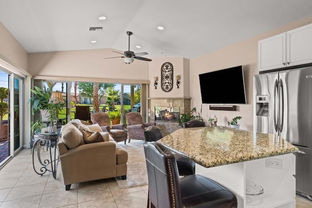 tiled living room with ceiling fan, vaulted ceiling, a fireplace, and a wealth of natural light