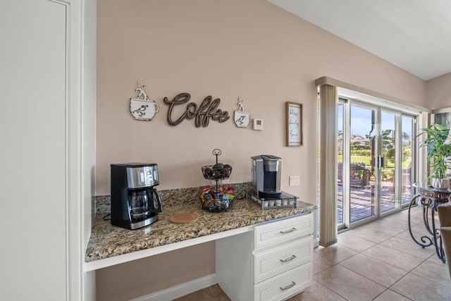 kitchen featuring light stone countertops, white cabinetry, light tile patterned floors, and built in desk