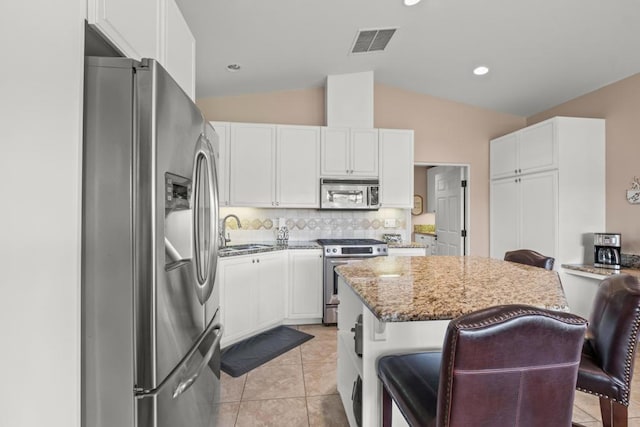 kitchen featuring lofted ceiling, stainless steel appliances, dark stone counters, sink, and a kitchen breakfast bar