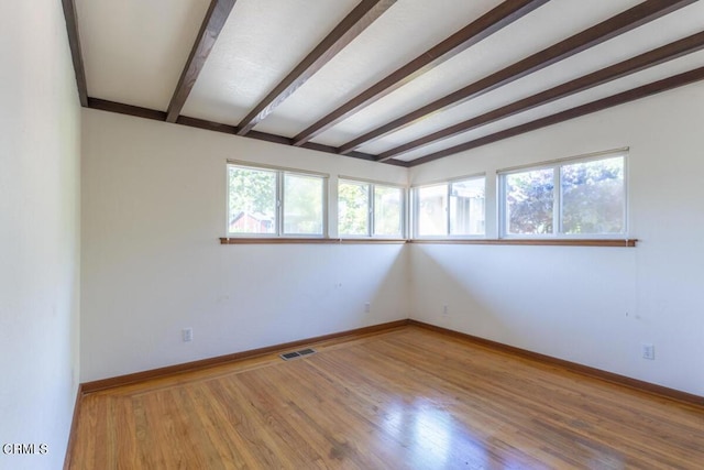 empty room with beam ceiling, hardwood / wood-style floors, and a healthy amount of sunlight