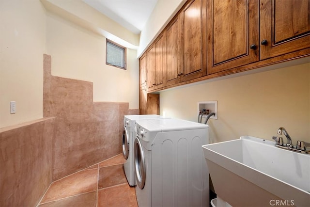 clothes washing area featuring light tile patterned floors, sink, washing machine and clothes dryer, and cabinets