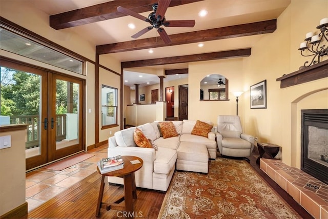 living room with french doors, a tiled fireplace, beam ceiling, and wood-type flooring