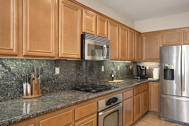 kitchen featuring light tile patterned floors, backsplash, stainless steel appliances, and dark stone counters