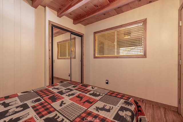 unfurnished bedroom with wood walls, beamed ceiling, a closet, wooden ceiling, and hardwood / wood-style floors