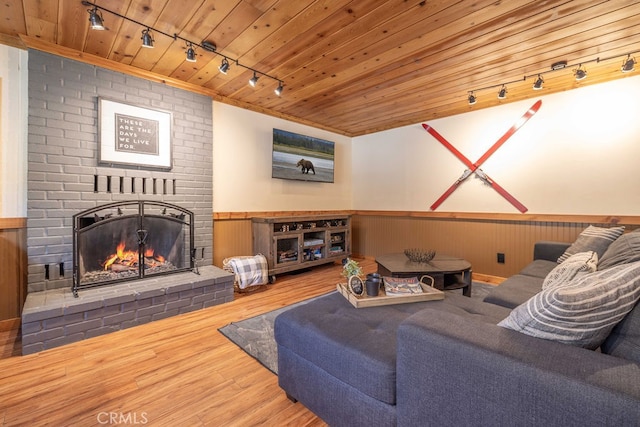 living room featuring rail lighting, wood ceiling, a fireplace, wood walls, and wood-type flooring