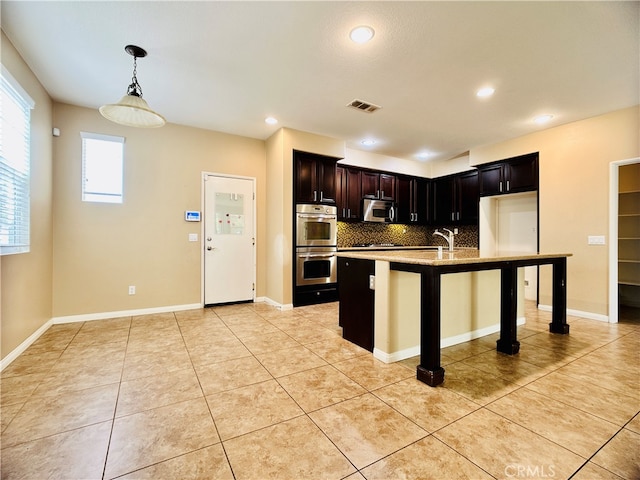 kitchen with tasteful backsplash, appliances with stainless steel finishes, hanging light fixtures, a breakfast bar area, and a kitchen island with sink