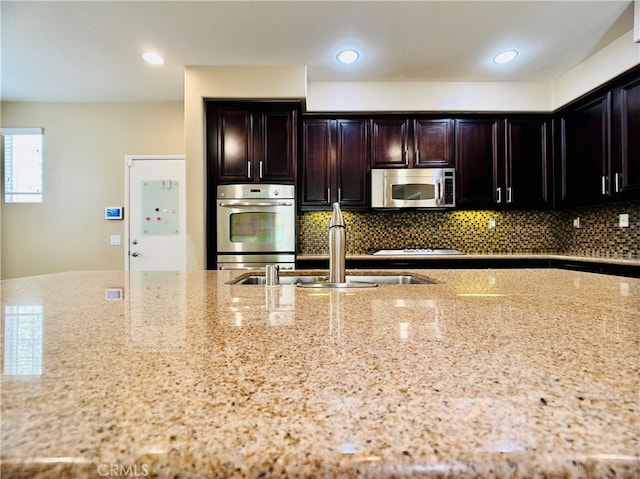 kitchen featuring light stone countertops, stainless steel appliances, dark brown cabinets, and backsplash