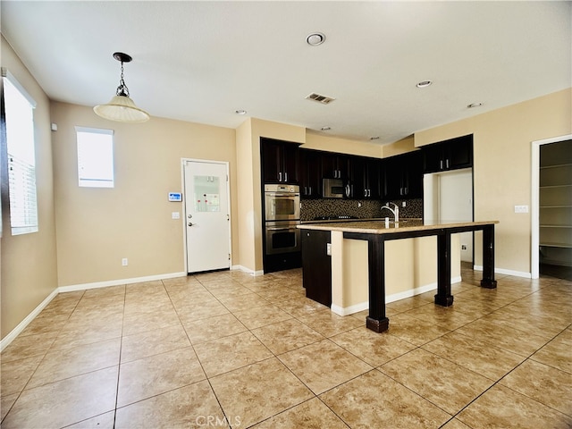 kitchen featuring tasteful backsplash, a center island with sink, a kitchen breakfast bar, stainless steel appliances, and decorative light fixtures