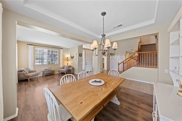 dining space with an inviting chandelier, a raised ceiling, and dark hardwood / wood-style floors