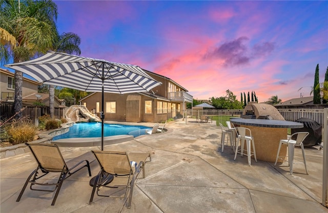 pool at dusk with a patio area and a bar