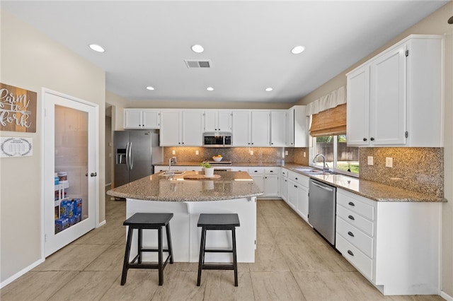 kitchen with stainless steel appliances, white cabinets, light stone counters, and a center island