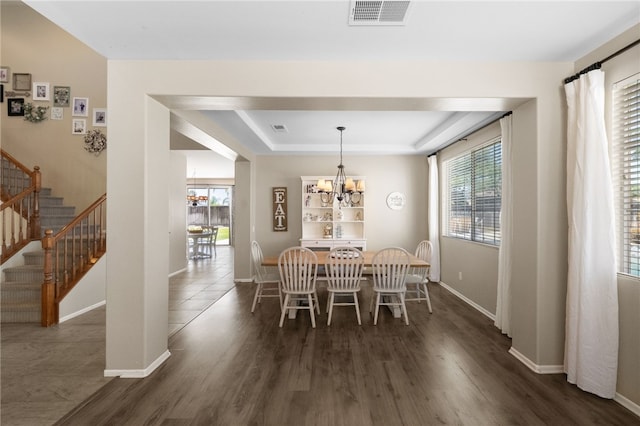 dining space with dark wood-type flooring, a raised ceiling, an inviting chandelier, and a wealth of natural light