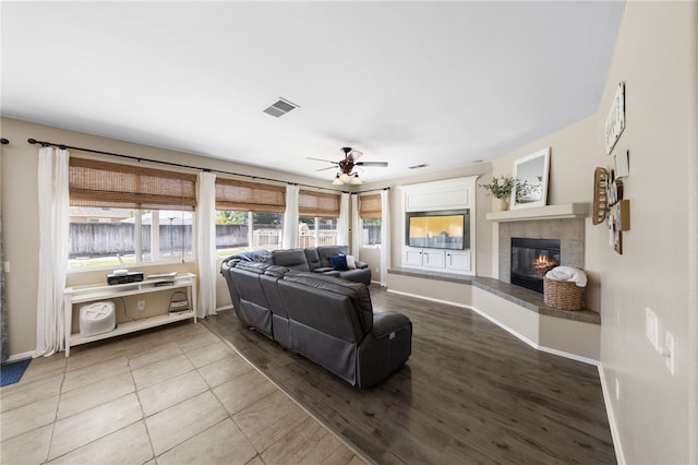 living room featuring ceiling fan, a tiled fireplace, and tile patterned flooring