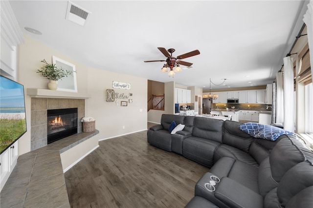 living room featuring ceiling fan with notable chandelier, a healthy amount of sunlight, a tile fireplace, and dark hardwood / wood-style flooring