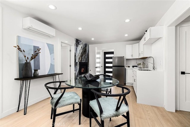 dining space with sink, a wall mounted AC, a fireplace, and light hardwood / wood-style flooring