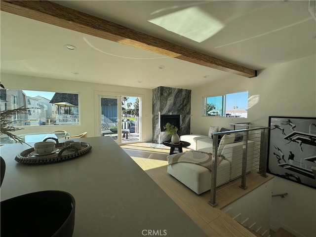 living room featuring beamed ceiling, a healthy amount of sunlight, and a premium fireplace