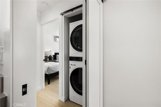 laundry area with light hardwood / wood-style flooring and stacked washing maching and dryer