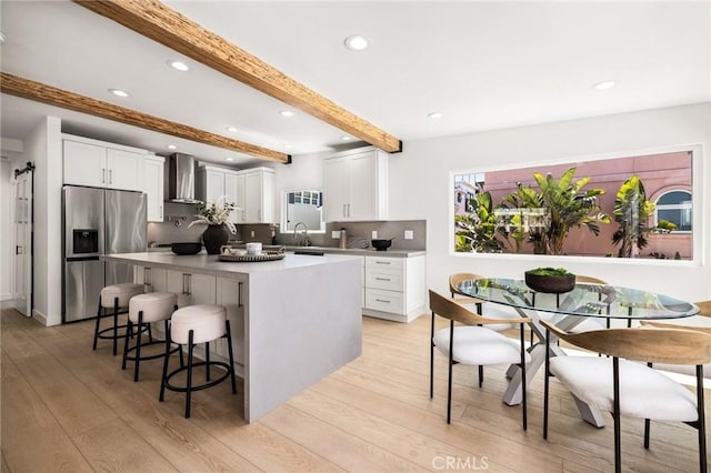 kitchen with a breakfast bar area, white cabinetry, a center island, stainless steel fridge with ice dispenser, and wall chimney range hood