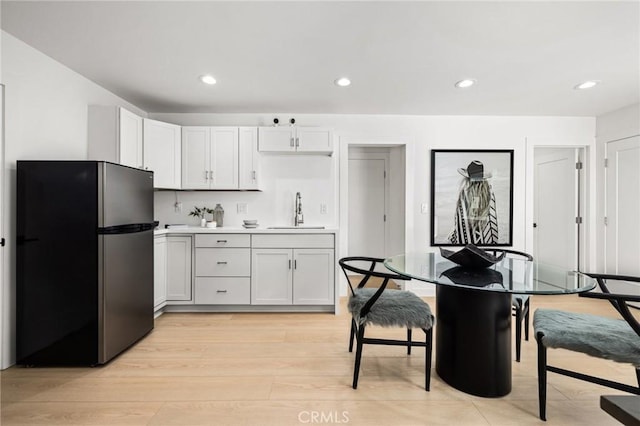 kitchen with stainless steel fridge, sink, light hardwood / wood-style flooring, and white cabinets